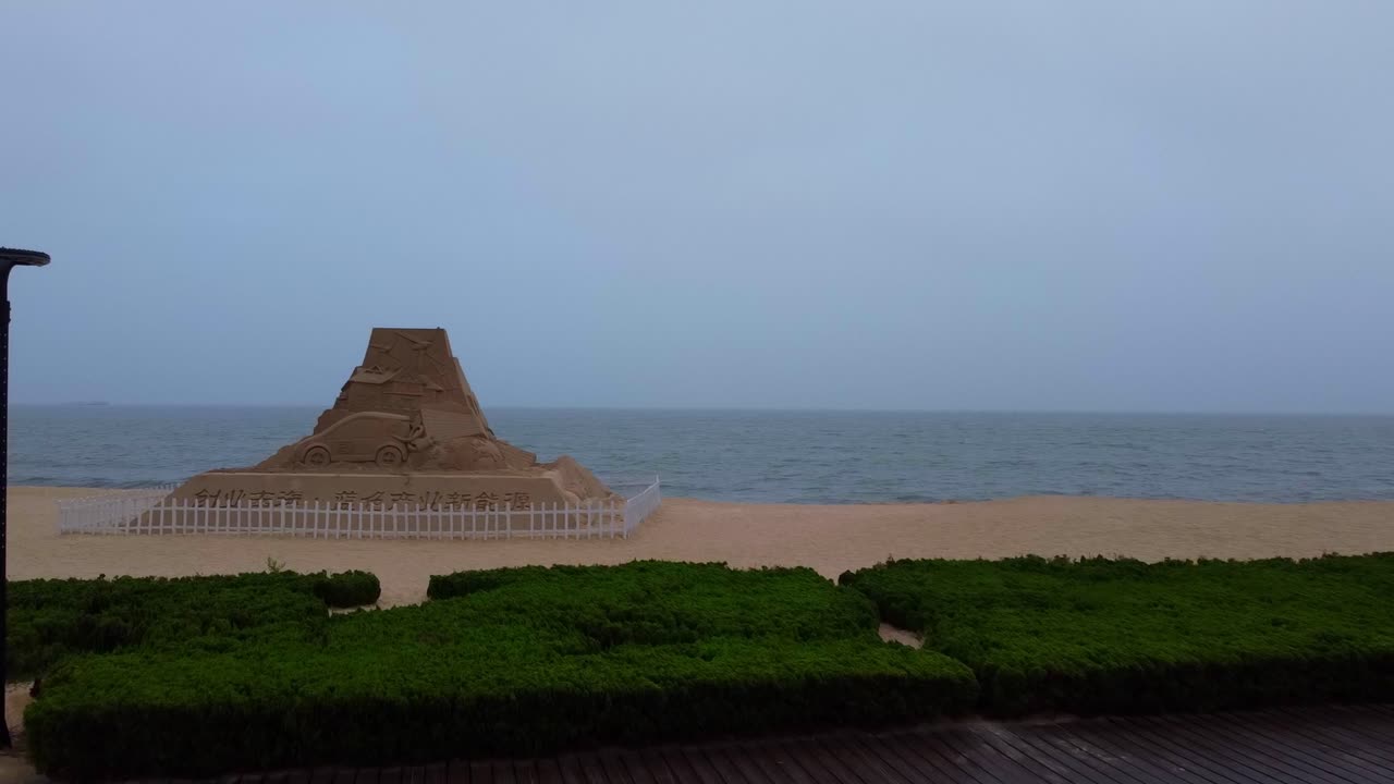 Aerial closeup dolly view of tall huge pyramid shaped sand sculpture revealing car charging and renewable energy