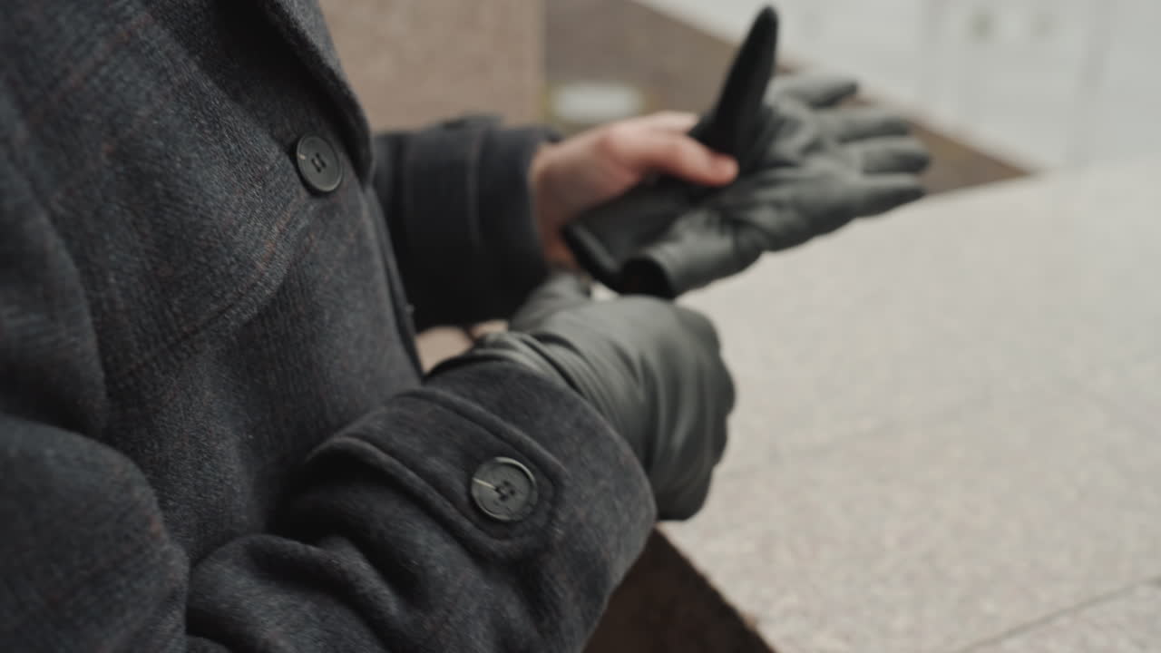 Man putting on leather gloves, coat urban granite ledge by wet pavement, beanie and scarf visible, moody cinematic closeups of hands and texture, quiet anticipation as creator prepares for outdoor