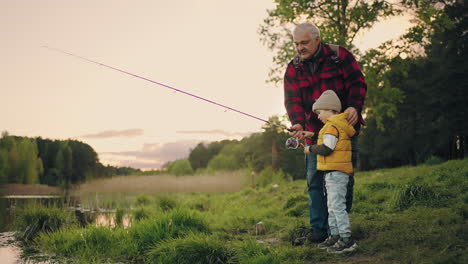 el niño feliz está pasando tiempo con el abuelo. el abuelo está enseñando al nieto a pescar.