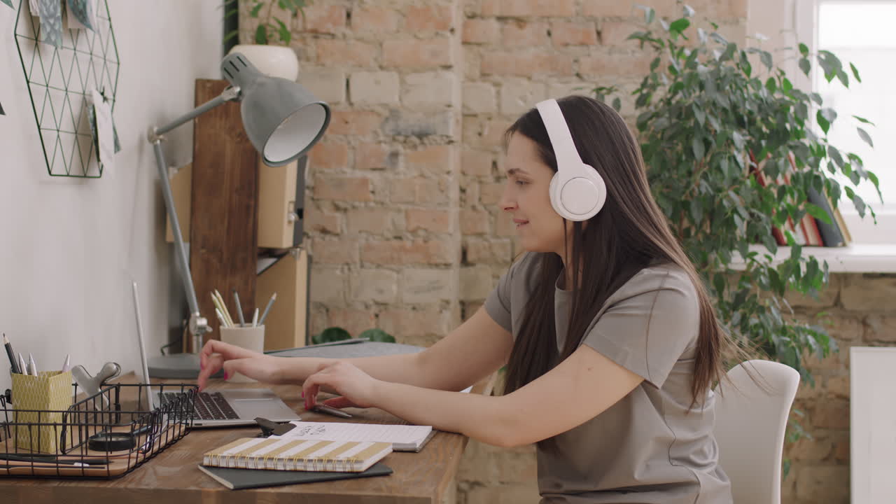 Woman in Headphones Listening to Music and Typing on Laptop