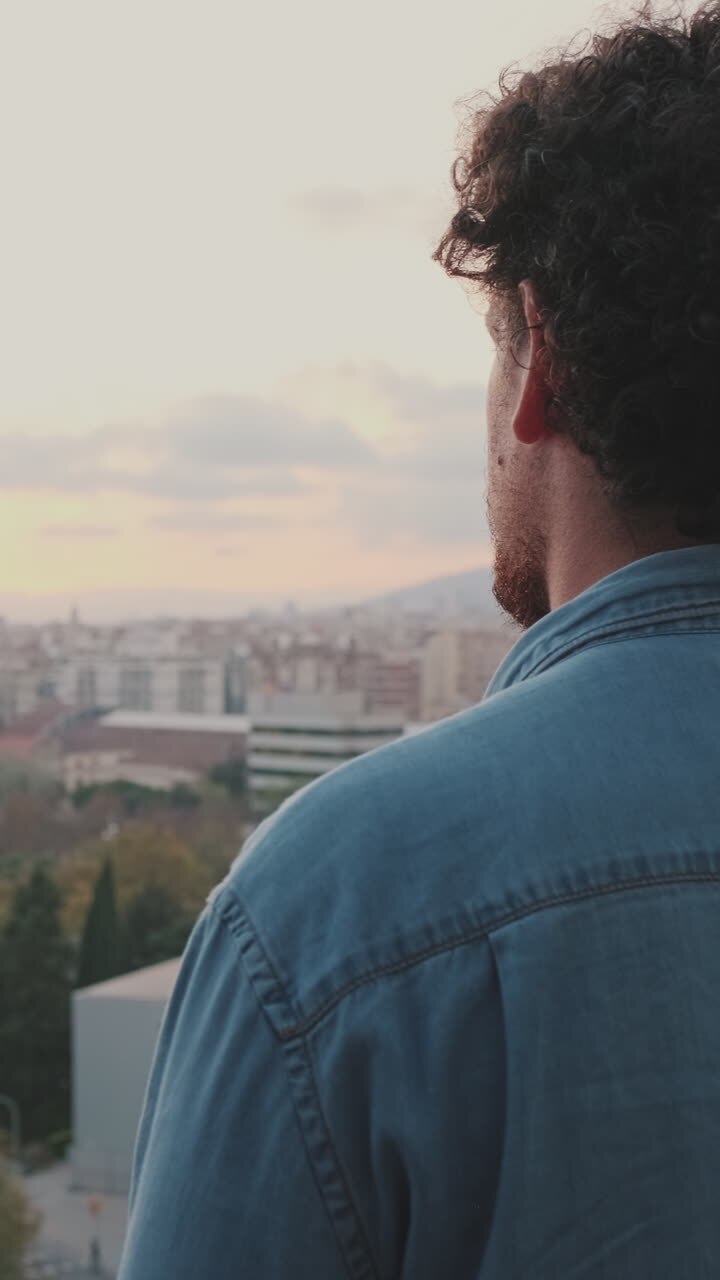 Man with Curly Hair Overlooking City at Sunset