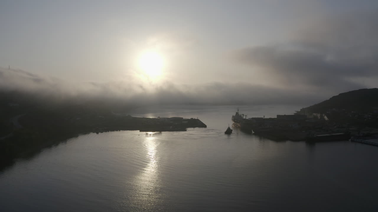 잔잔한 물이 있는 만 위를 날고, 태양은 물 표면에 반사되고, 언덕 너머에서 오는 짙은 안개 구름, 일몰