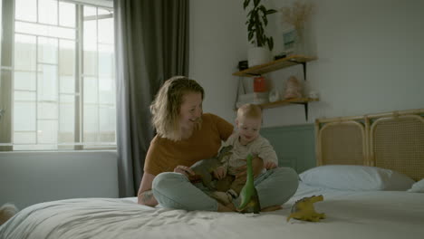 mutter und baby spielen mit dinosauriern auf einem bett