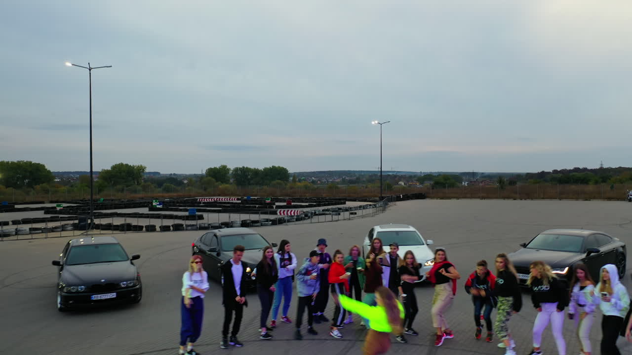 Bunch of youngsters dancing on the square at daytime. Teenagers having fun performing hip hop. Few cars at backdrop. Top view.