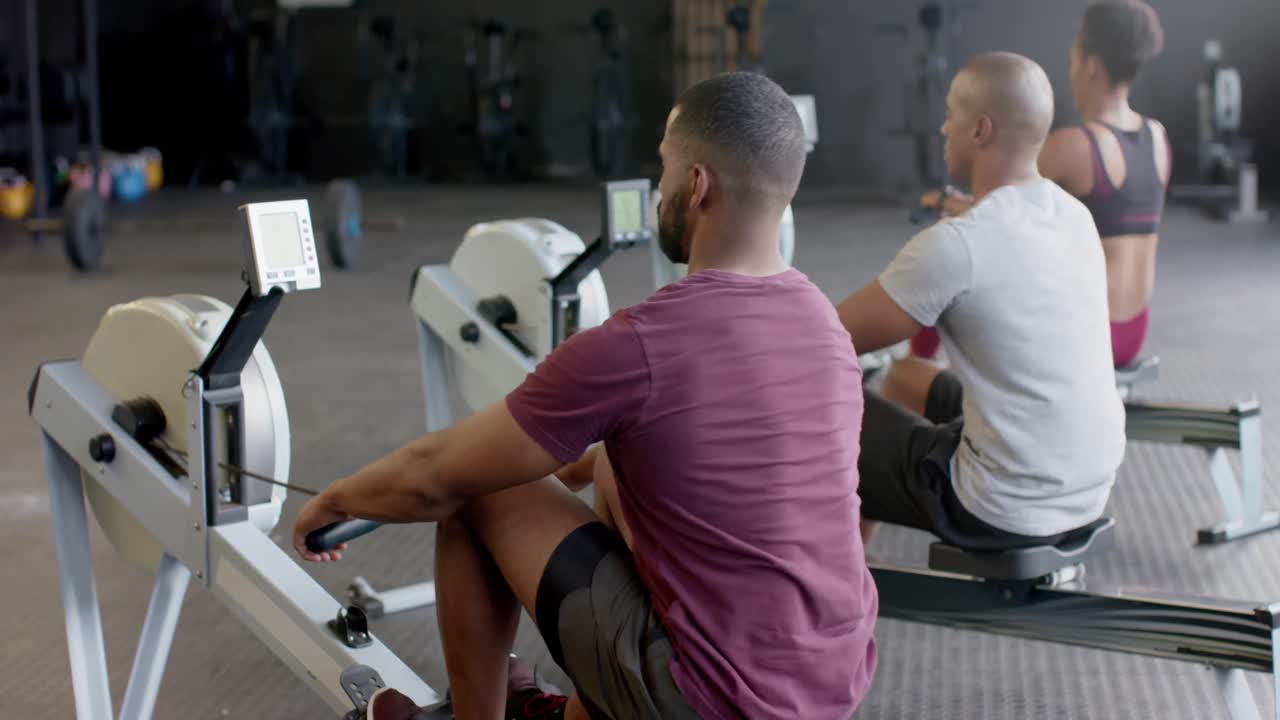 Rear view of diverse group fitness class training hard on rowing machines at gym, in slow motion