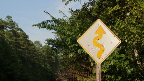 a medium shot of a road warning sign that has been vandalized by multiple gun shots along a rural road in the ouachita national forest arkansas