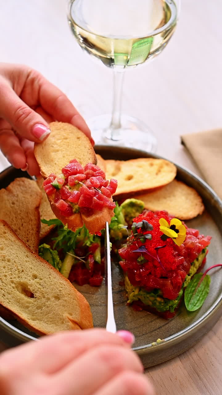 Mano che serve tartare di tonno su pane tostato. Persona che spalma la tartare di tonno su pane tostato accanto a un bicchiere di vino bianco in un ristorante.