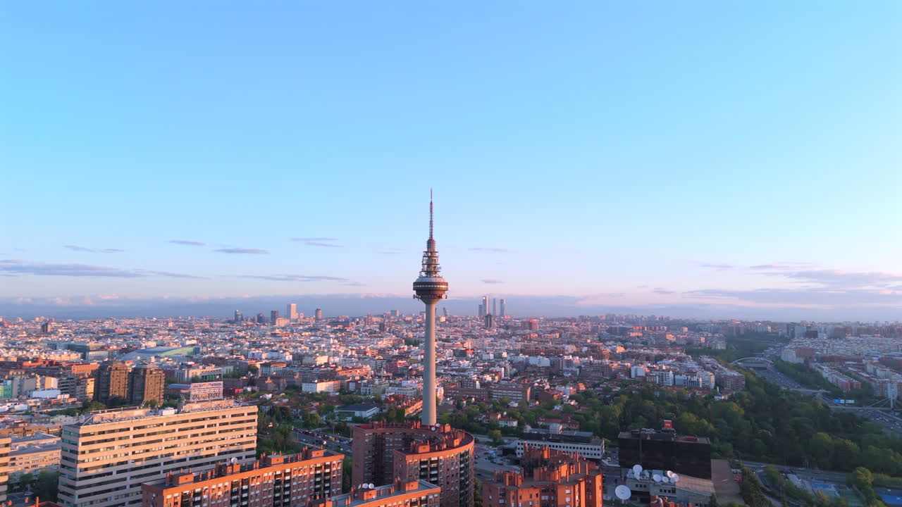 Aerial drone orbit around Madrid's iconic TV tower at sunrise, showcasing stunning golden light on city skyline. Perfect for urban projects, tourism, documentaries, and landmark promotions
