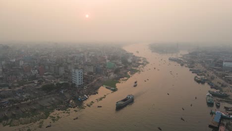 river through city with cargo ship and buildings - aerial establishing shot with rising sun in foggy morning