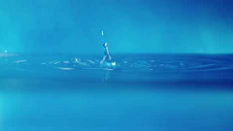 vídeo en 4k en cámara lenta de una superficie de agua con gotas que caen sobre un fondo azul. salpicaduras de agua. rodaje de estudio.