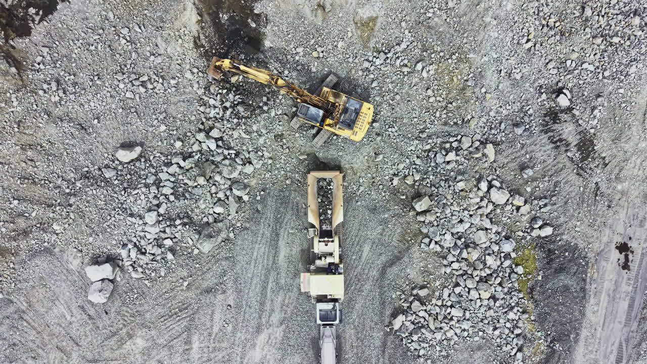 Heavy machinery working at a granite quarry site during daylight hours, showing equipment and rock piles