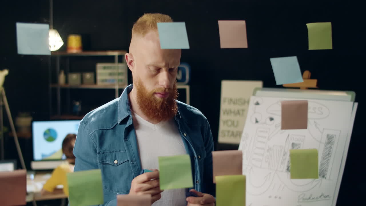 Closeup focused hipster guy making tick on stickers with marker in night office