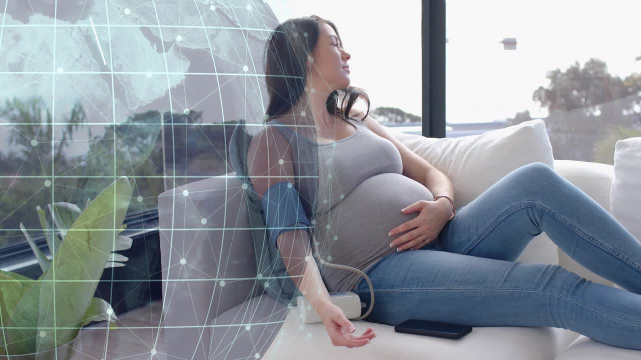 Pregnant mom on sofa placing cuff tapping monitor checking BP while holo grid overlapping sofa