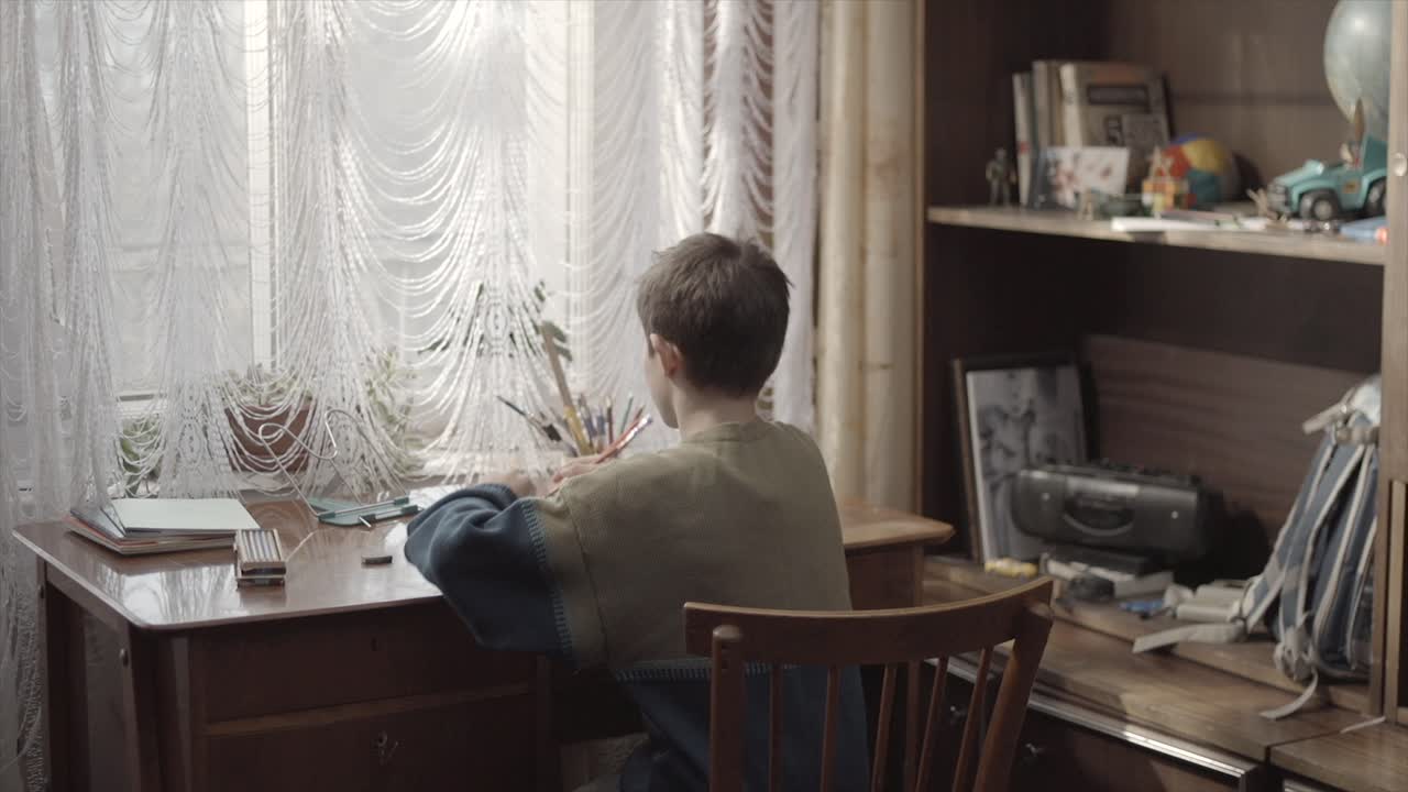 Boy Doing Homework at a Wooden Desk by the Window