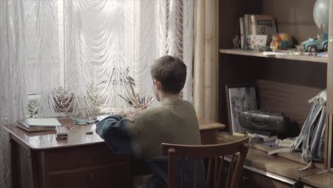 boy doing homework at a wooden desk by the window