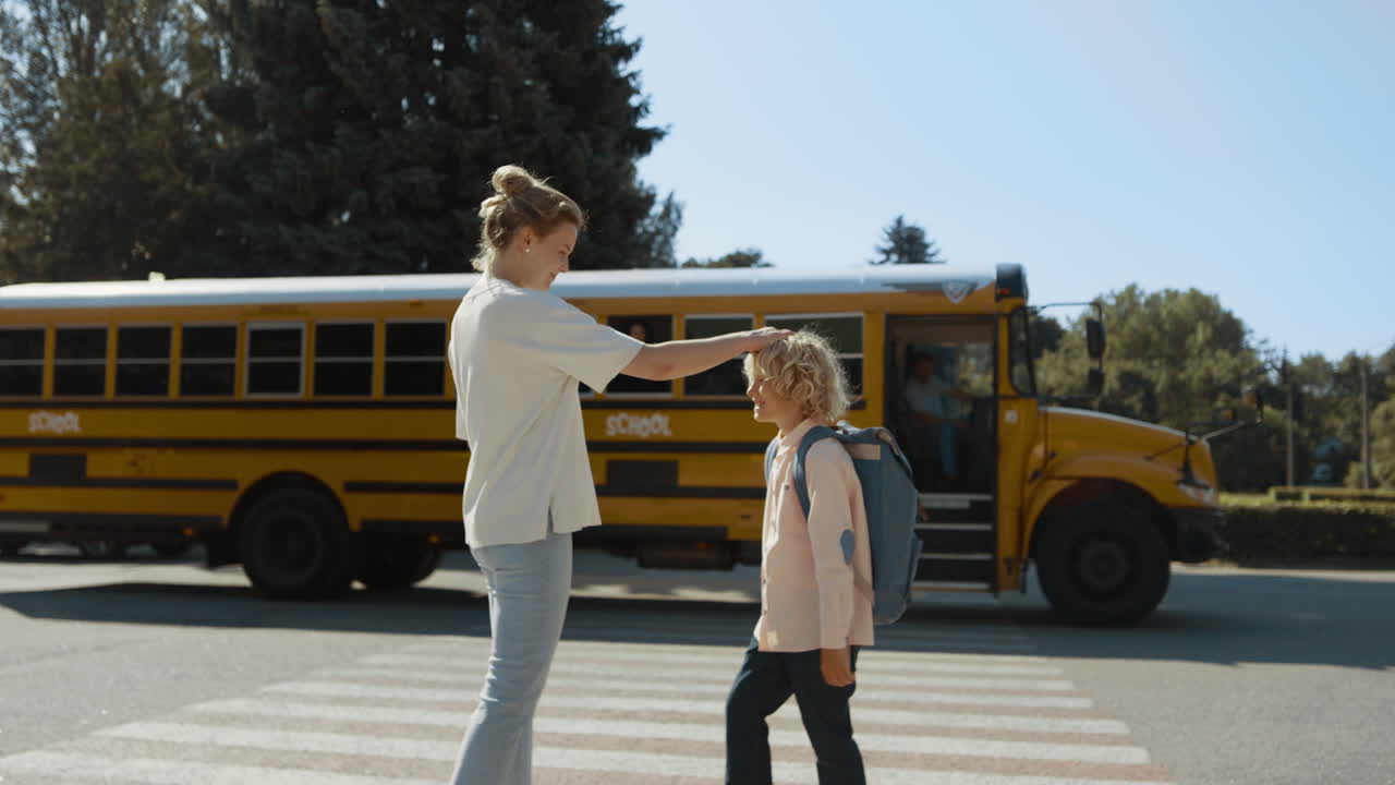 Zorgzame moeder begeleidt zoon naar de schoolbus. Moeder kijkt hoe kind in de schoolbus stapt.