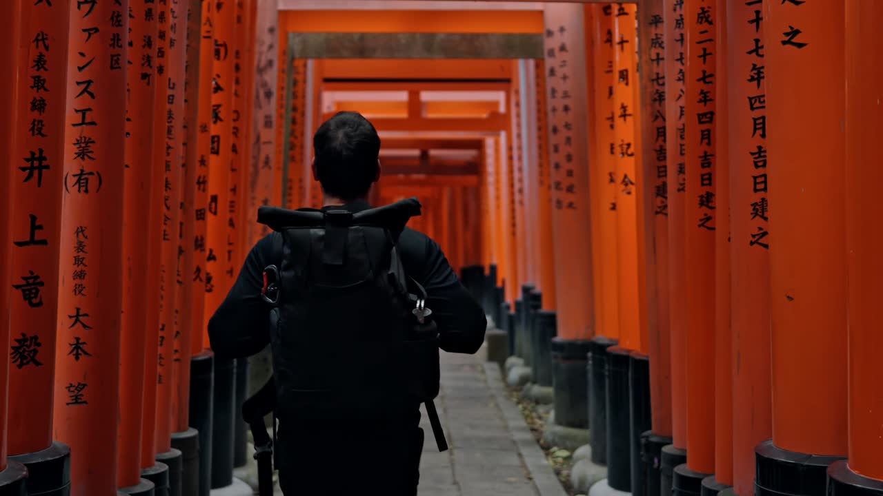 A mesmerizing scene of a man walking through the endless red torii gates of Fushimi Inari Shrine in Kyoto, Japan.