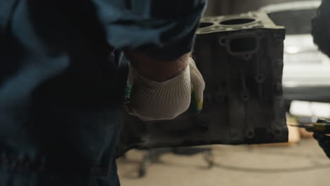 close-up of mechanic in blue uniform using yellow scraper on car engine while another mechanic in white gloves loosens bolt, working together in busy automotive workshop