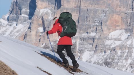 Man-walking-up-steep-snowy-slope-with-large-mountain-in-the-background-slow-motion