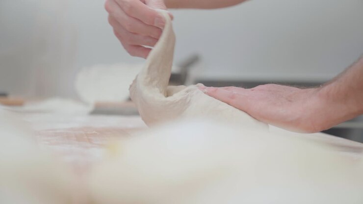 Baker kneading and folding dough to prepare pie in a bakery