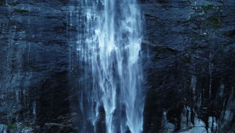 ascending shot of smooth waterfall crashing down rocky mountain wall in norway