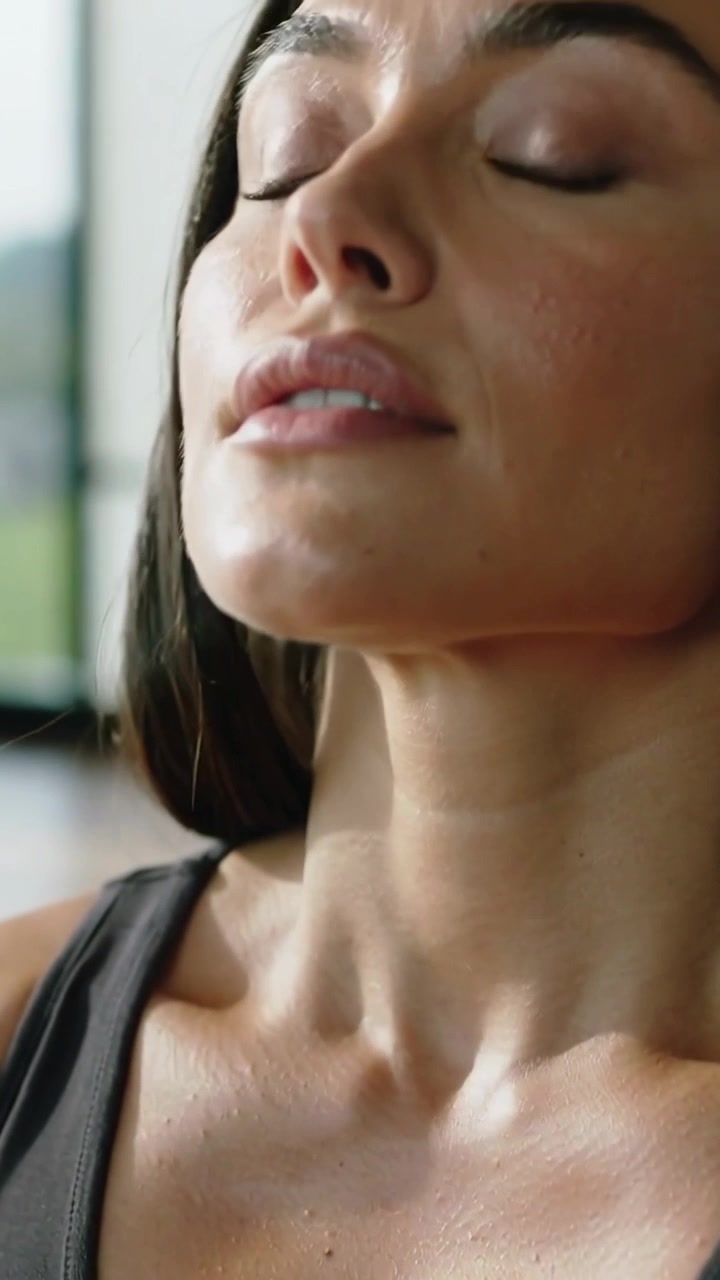 Video verticale: Donna affannata in palestra con canotta scura dopo una serie, che inclina la testa all'indietro, mostrando il sudore.