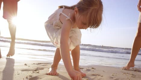 Glückliche-Familie,-Die-Am-Strand-Spielt-Und-Bei-Sonnenuntergang-Im-Sand-Zeichnet