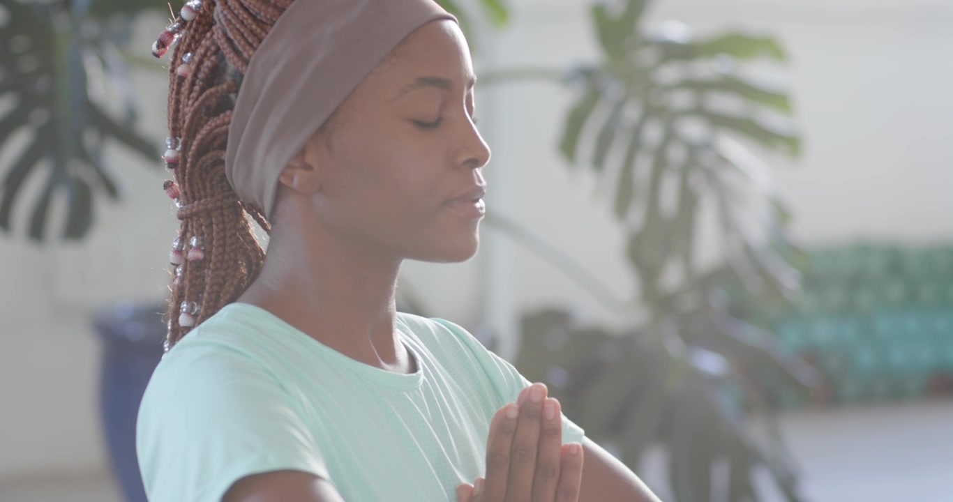 Adult African woman starting prayer pose, eyes-closing, meditating in studio with mint shirt, watch
