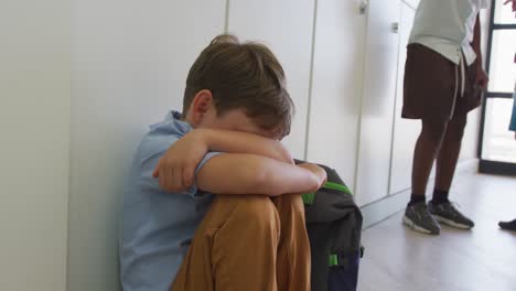 video de un triste niño caucásico sentado en el pasillo de la escuela, cubriendo la cabeza con las manos