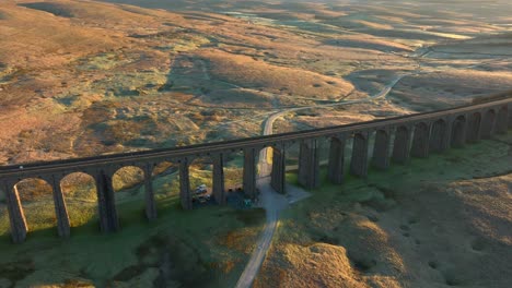 arched railway bridge viaduct spanning bare moorland with dirt track at sunrise in winter