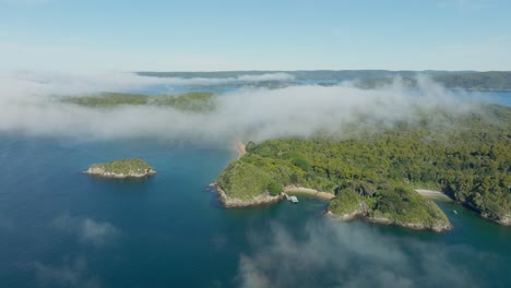 Stunning-aerial-view-of-Ulva-Island-with-fluffy-clouds-on-a-sunny-day-with-calm-placid-ocean-water-within-Paterson-Inlet,-part-of-Stewart-Island-Rakiura-in-the-south-of-New-Zealand-Aotearoa