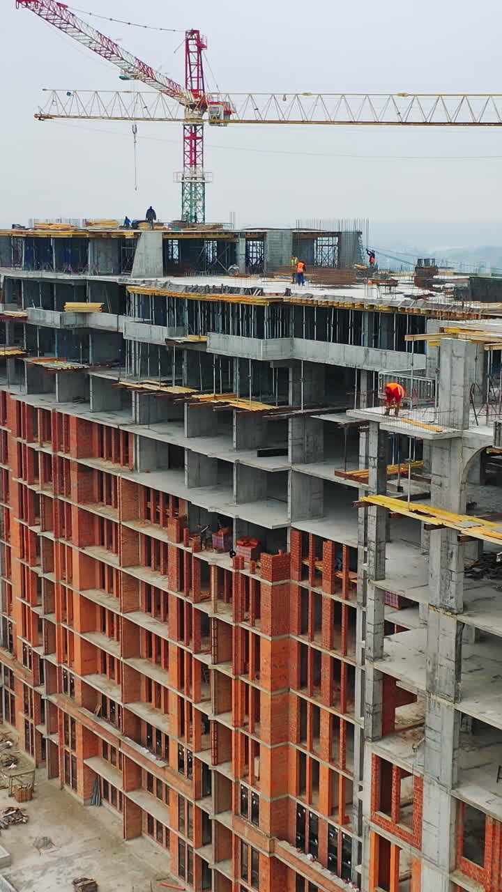 Construction site of modern skyscraper. Aerial side view on a new high-rise building in a new residential complex of a megacity. Vertical video