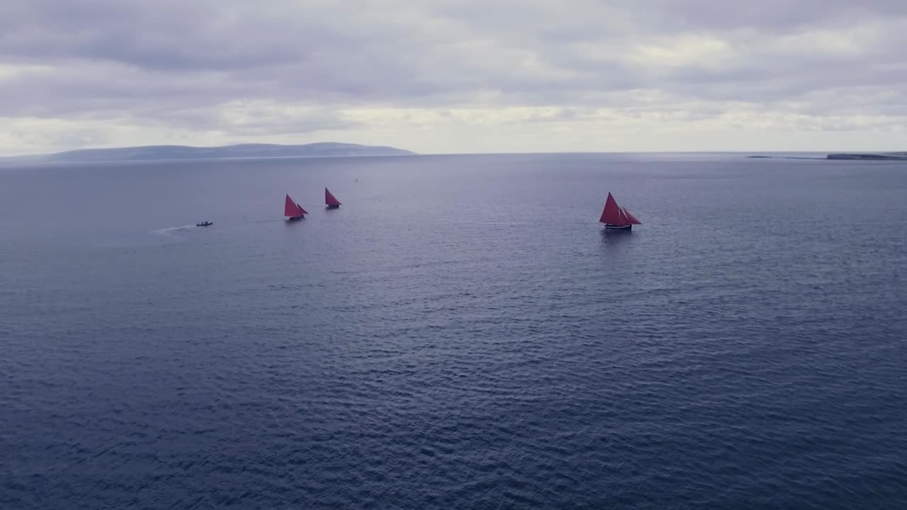 toma aérea de tres barcos con velas rojas saliendo al mar