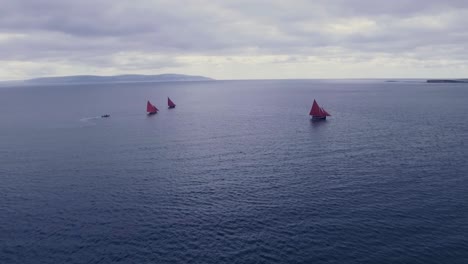 aerial shot of three boats with red sails moving out to sea