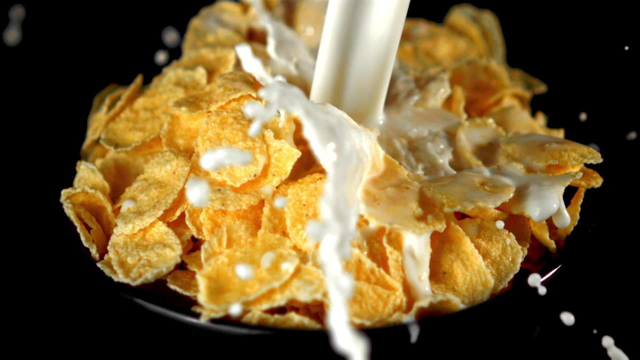 Milch gießt in Zeitlupe über goldene Cornflakes.