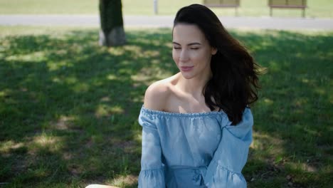 Portrait-of-attractive-brunette-woman-in-blue-dress-sitting-in-a-park