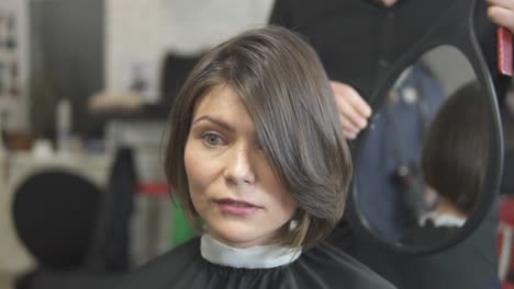 Peluquero-Profesional-Usando-Un-Espejo-Para-Mostrar-Su-Corte-De-Pelo-A-Un-Cliente.-Mujer-Joven-Vistiéndose-El-Pelo-En-El-Salón