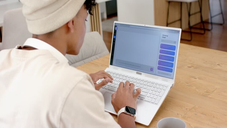 African American man typing on white laptop at home, pausing on blue bubble, replying, copy space