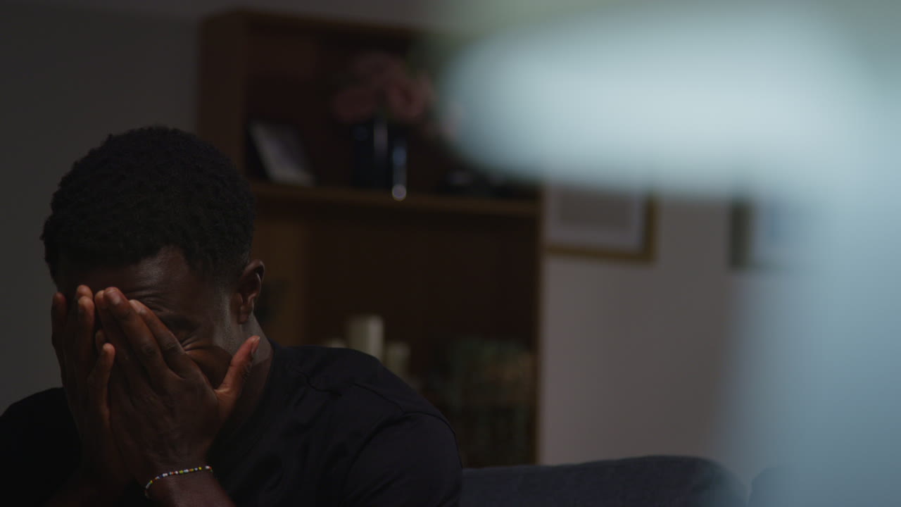 Unhappy And Depressed Young Man Sitting On Sofa At Home At Night Shaking Head