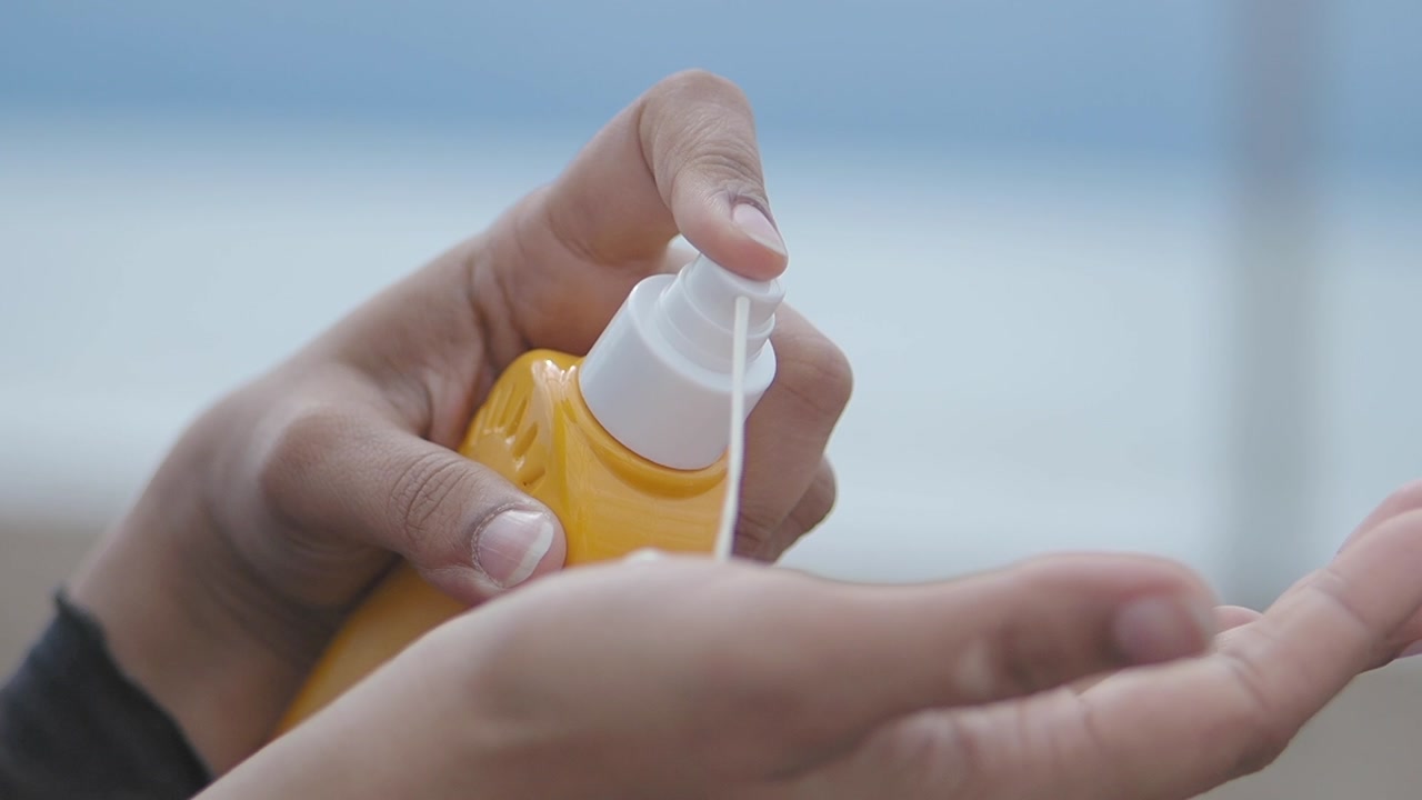 Close-up of Hands Dispensing Sunscreen Lotion from a Yellow Pump Bottle