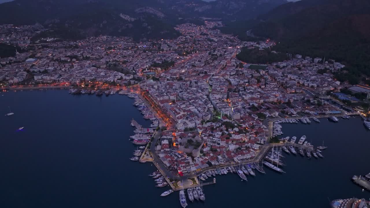 Aerial view of Marmaris harbor, boats, and sunrise-lit mountains, Turkey