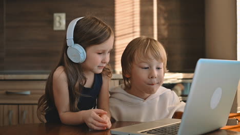 Little-Girl-And-Boy-Using-A-Laptop-With-Wireless-Headphones-And-Having-An-Online-Class-At-Home