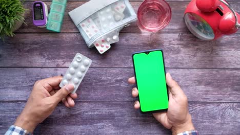 close up of hand holding blister packs and using smart phone on table