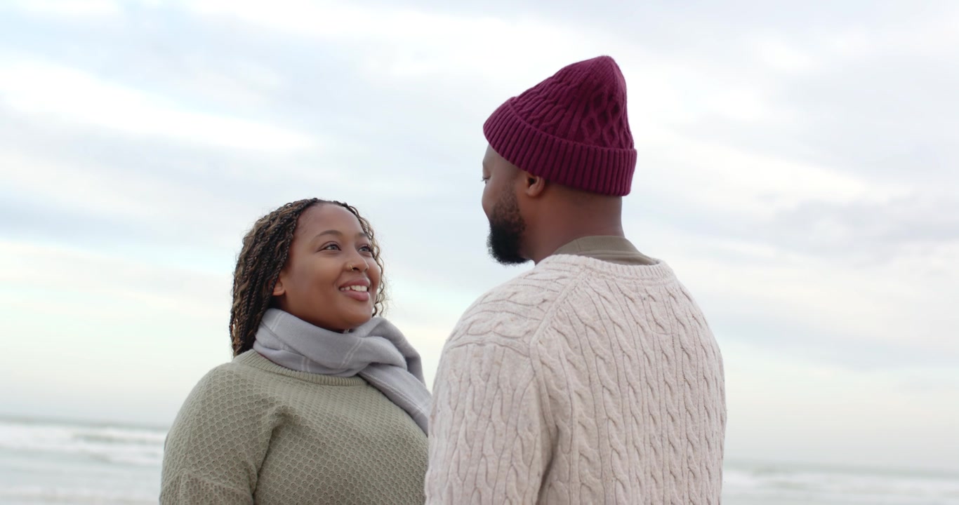 African American couple beach woman looking up sharing affection man listening knits scarf hat sea