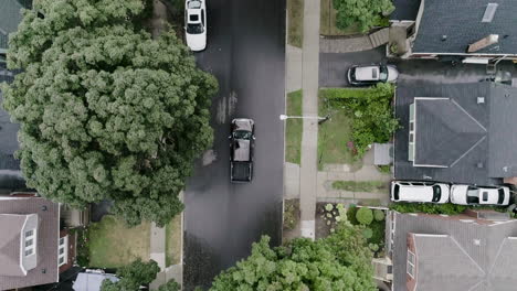 Aerial-shot-of-large-truck-driving-through-residential-neighborhood-with-houses-and-trees