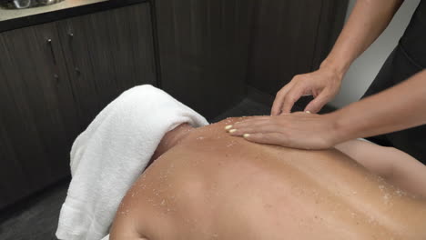 masajista mano hace un masaje exfoliante de sal en la parte posterior de la persona