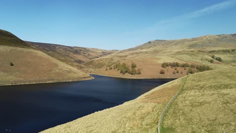 aerial shot of kinder reservoir with geese on the water and people in the distance walking on the other side and the valley climb up the kinder scout peak, peak district, uk