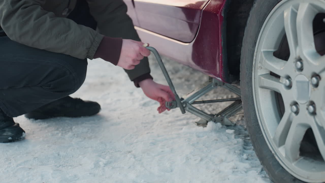 Close-up of auto engineer using spanner on jack, raising car on snowy ground, followed by hand adjustment on jack for further lifting, snowy winter scene, focusing on precise mechanical work