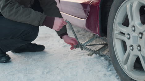 close-up of auto engineer using spanner on jack, raising car on snowy ground, followed by hand adjustment on jack for further lifting, snowy winter scene, focusing on precise mechanical work