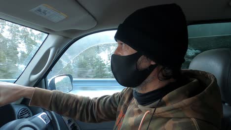 interior of a car with a man wearing a cloth mask as he drives in the snow during the covid-19 pandemic